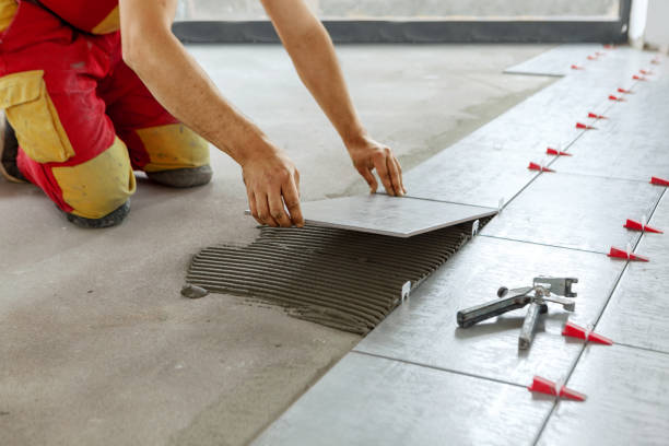 A person laying tiles on a floor, using a trowel to spread adhesive.