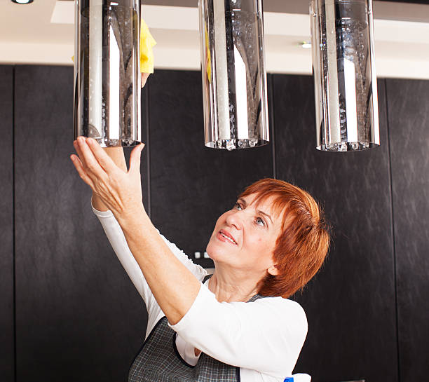A person cleaning a chandelier in the kitchen with a soft cloth.